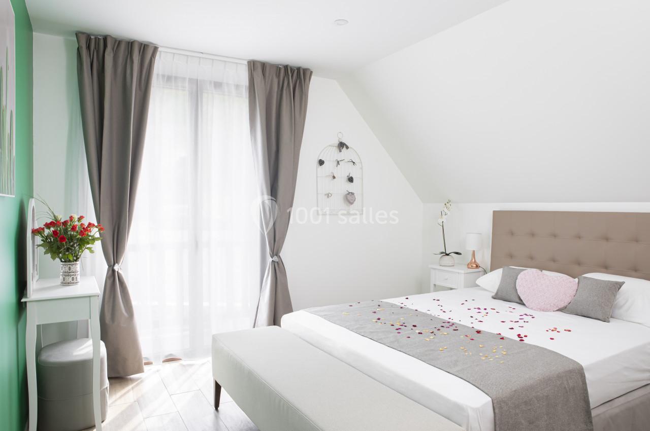 Location salle Saint-Samson-de-la-Roque (Eure) - Manoir Néo Normand #66 Chambre lumineuse avec lit double, draps décorés de pétales, rideaux gris, bureau avec vase de fleurs et lumière naturelle.