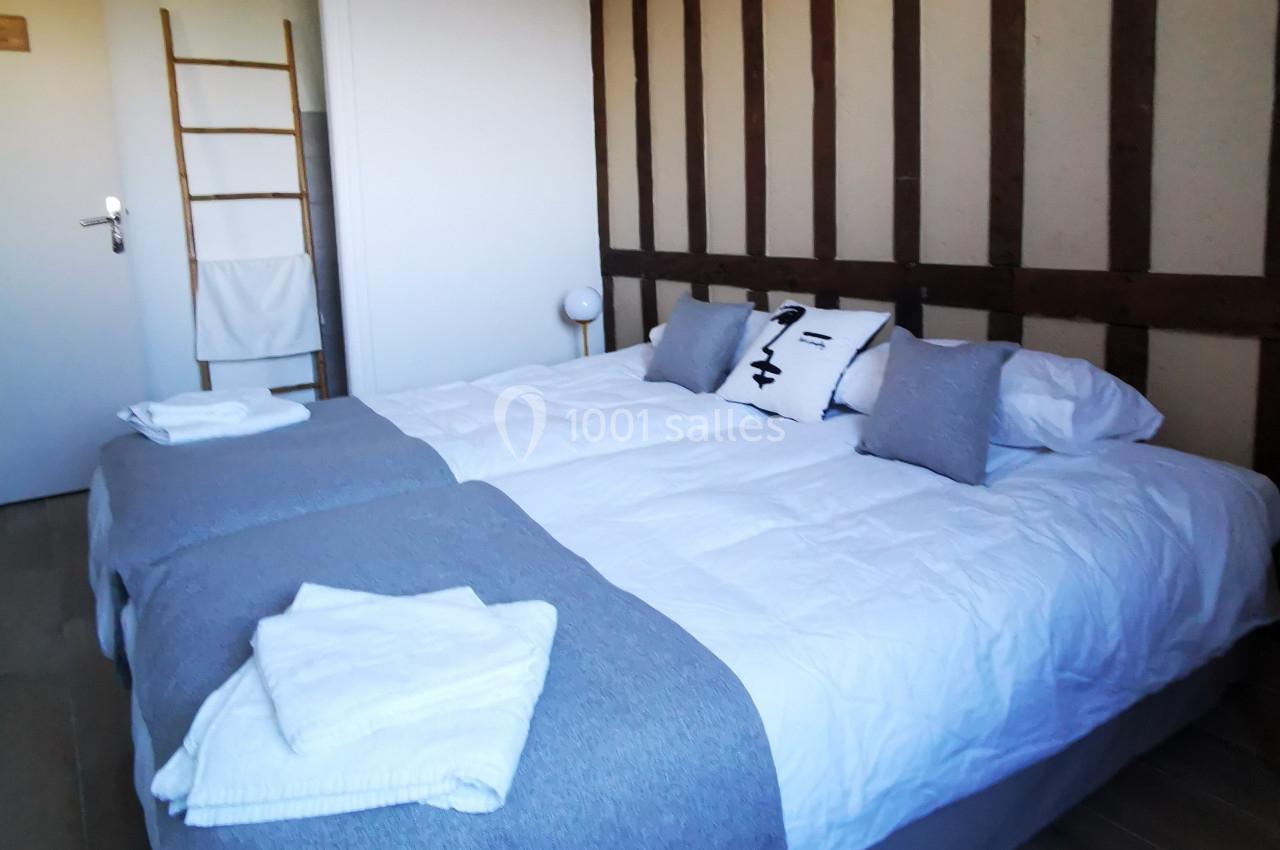 Location salle Saint-Samson-de-la-Roque (Eure) - Manoir Néo Normand #63 Lit double avec draps blancs, couvertures grises, coussins décoratifs et mur à colombages dans une chambre lumineuse.