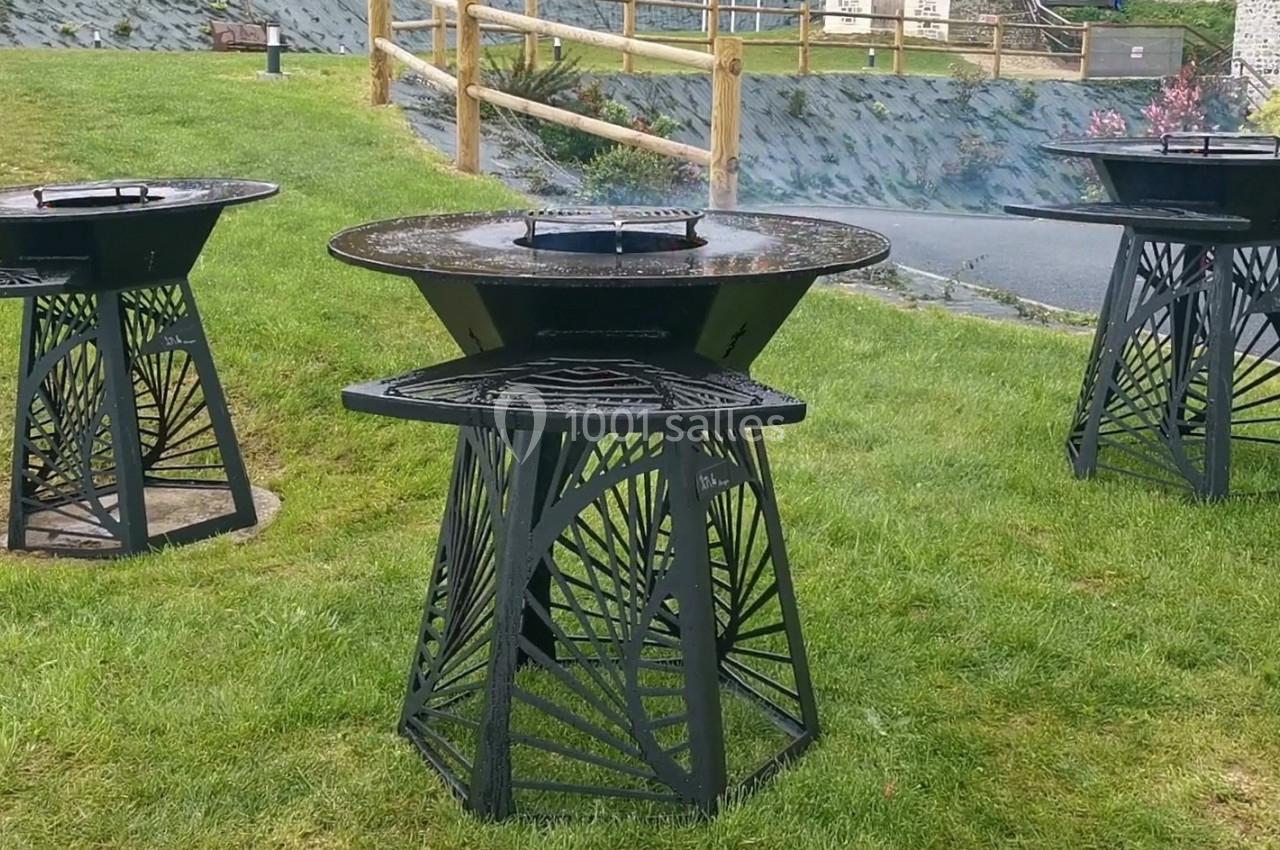 Location salle Saint-Samson-de-la-Roque (Eure) - Manoir Néo Normand #40 Trois braseros modernes en métal noir installés sur une pelouse, avec une clôture en bois en arrière-plan.