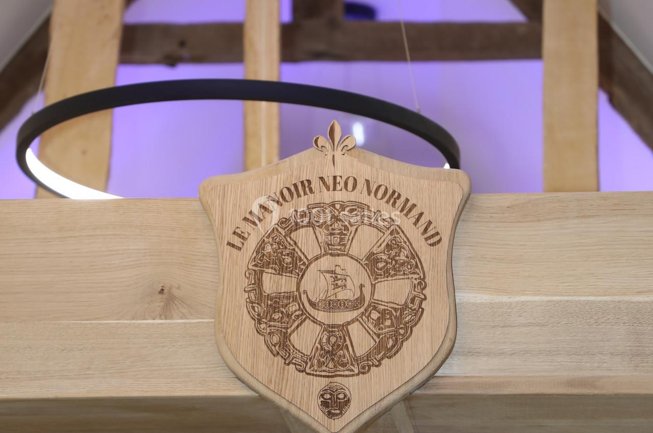 Location salle Saint-Samson-de-la-Roque (Eure) - Manoir Néo Normand #50 Blason en bois gravé ’Le Manoir Néo-Normand’ suspendu dans un intérieur avec poutres apparentes et éclairage moderne.