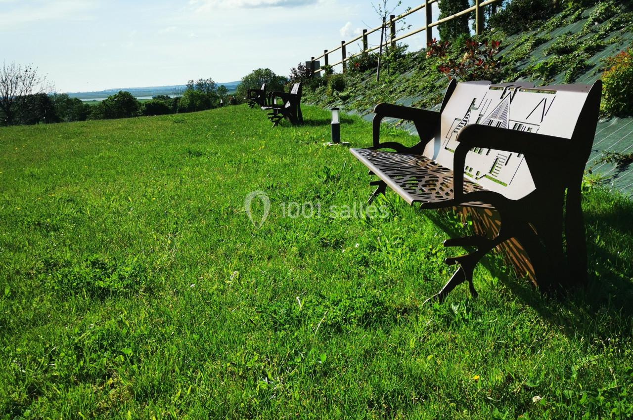 Location salle Saint-Samson-de-la-Roque (Eure) - Manoir Néo Normand #32 Bancs en bois alignés sur une pelouse verdoyante avec vue dégagée sur un paysage rural et ciel bleu.