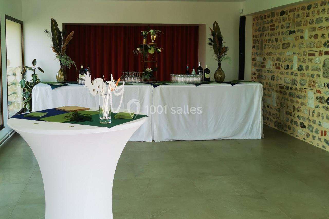 Location salle Saint-Samson-de-la-Roque (Eure) - Manoir Néo Normand #45 Salle de réception avec table haute en premier plan et buffet décoré de plantes et nappes blanches en arrière-plan.