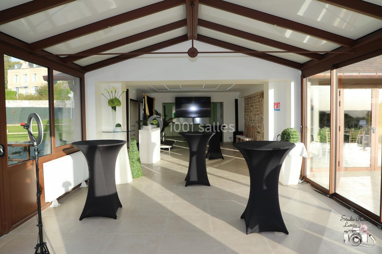 Location salle Saint-Samson-de-la-Roque (Eure) - Manoir Néo Normand #51 Salle lumineuse avec tables hautes noires, grandes baies vitrées, écran au fond et vue sur un jardin.