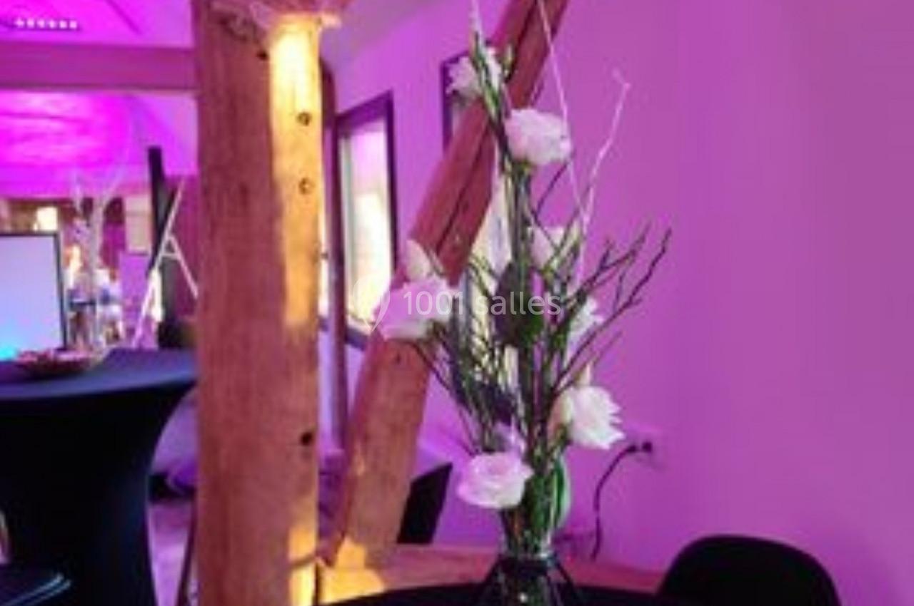 Location salle Saint-Samson-de-la-Roque (Eure) - Manoir Néo Normand #47 Vase en verre avec des fleurs blanches et des branches décoratives sur une table noire, dans une salle éclairée en rose.