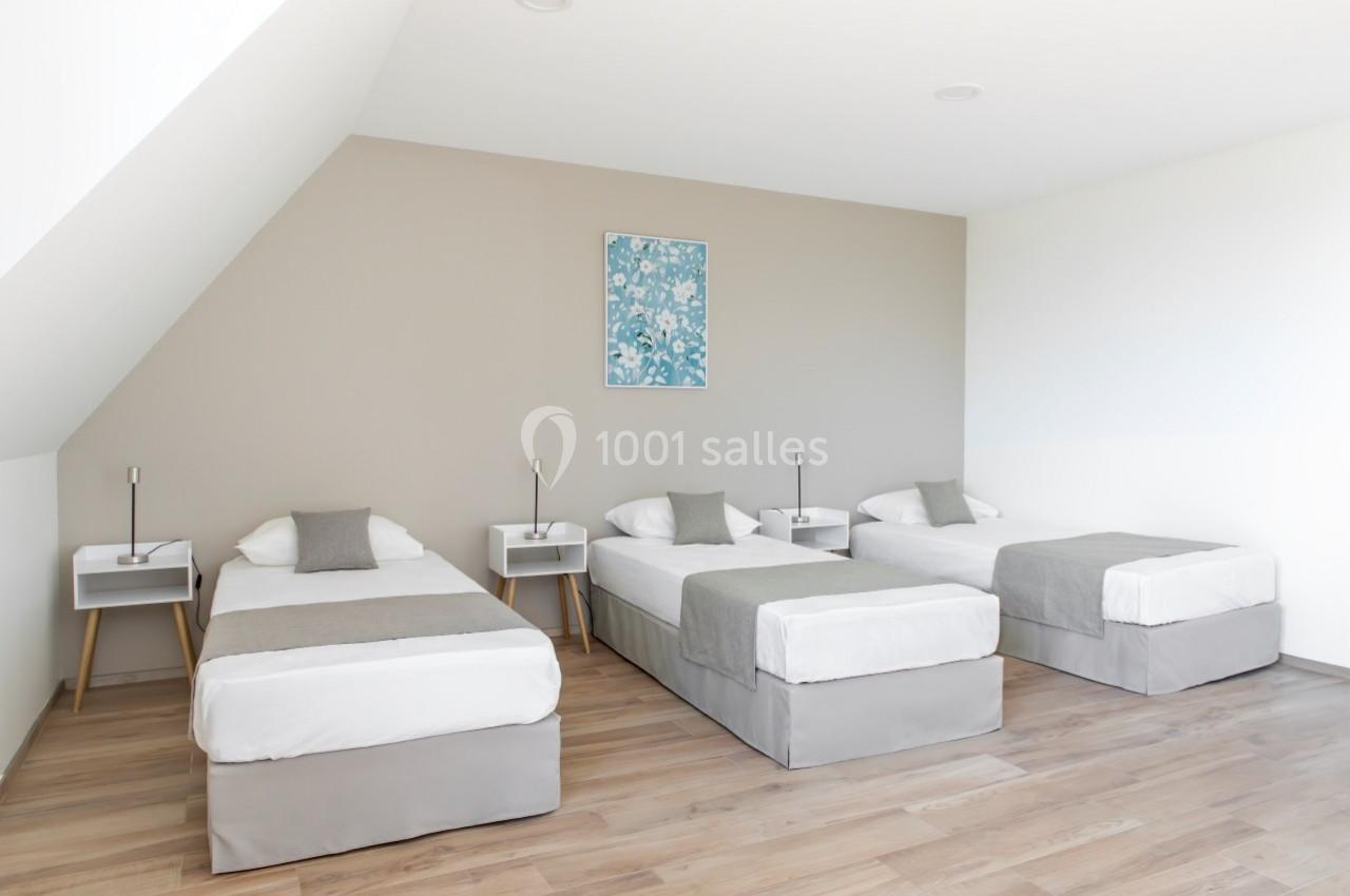 Location salle Saint-Samson-de-la-Roque (Eure) - Manoir Néo Normand #69 Trois lits simples alignés dans une chambre lumineuse avec parquet et mur beige décoré d'un tableau floral.