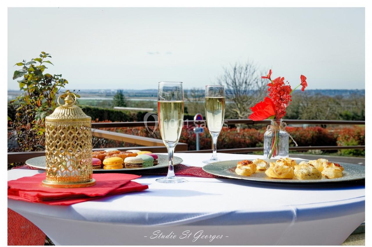 Location salle Saint-Samson-de-la-Roque (Eure) - Manoir Néo Normand #73 Table dressée en extérieur avec macarons, amuse-bouches, deux verres de champagne et un vase de fleurs rouges.