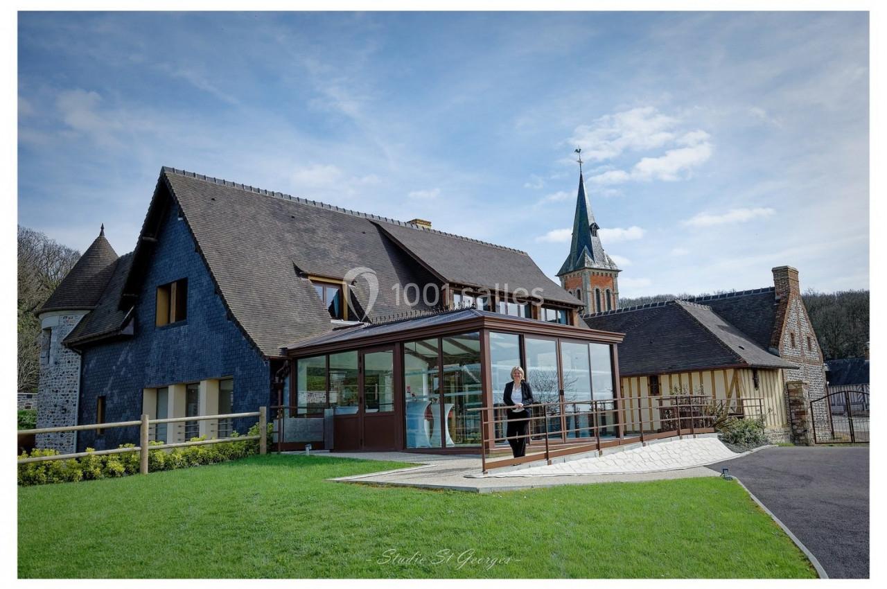 Location salle Saint-Samson-de-la-Roque (Eure) - Manoir Néo Normand #74 Maison traditionnelle avec toit en ardoise, véranda moderne et jardin, située près d'une église avec clocher.