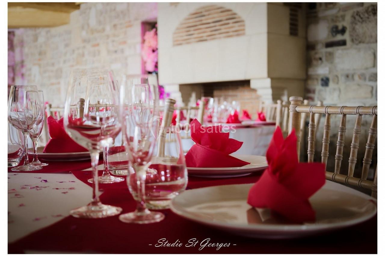 Location salle Saint-Samson-de-la-Roque (Eure) - Manoir Néo Normand #75 Table dressée avec nappes rouges, serviettes pliées en éventail, verres et assiettes, devant une cheminée en pierre.