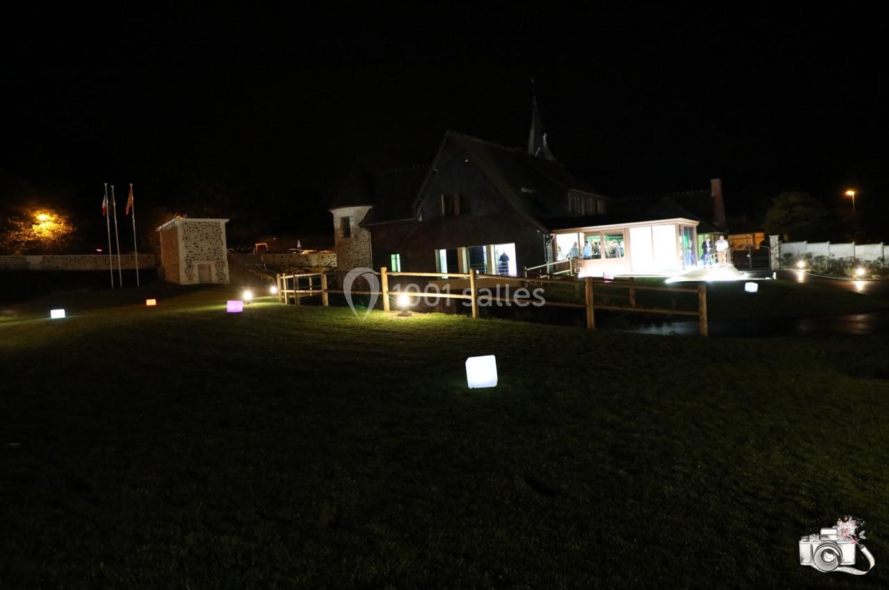 Location salle Saint-Samson-de-la-Roque (Eure) - Manoir Néo Normand #84 Bâtiment éclairé de nuit avec des cubes lumineux colorés sur une pelouse et des drapeaux en arrière-plan.