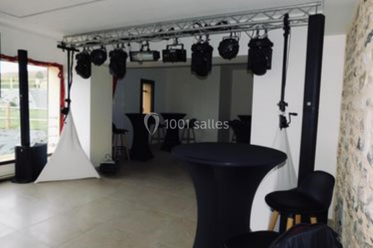 Location salle Saint-Samson-de-la-Roque (Eure) - Manoir Néo Normand #89 Salle équipée de tables hautes, chaises noires et éclairages suspendus, avec un mur en pierre apparente.