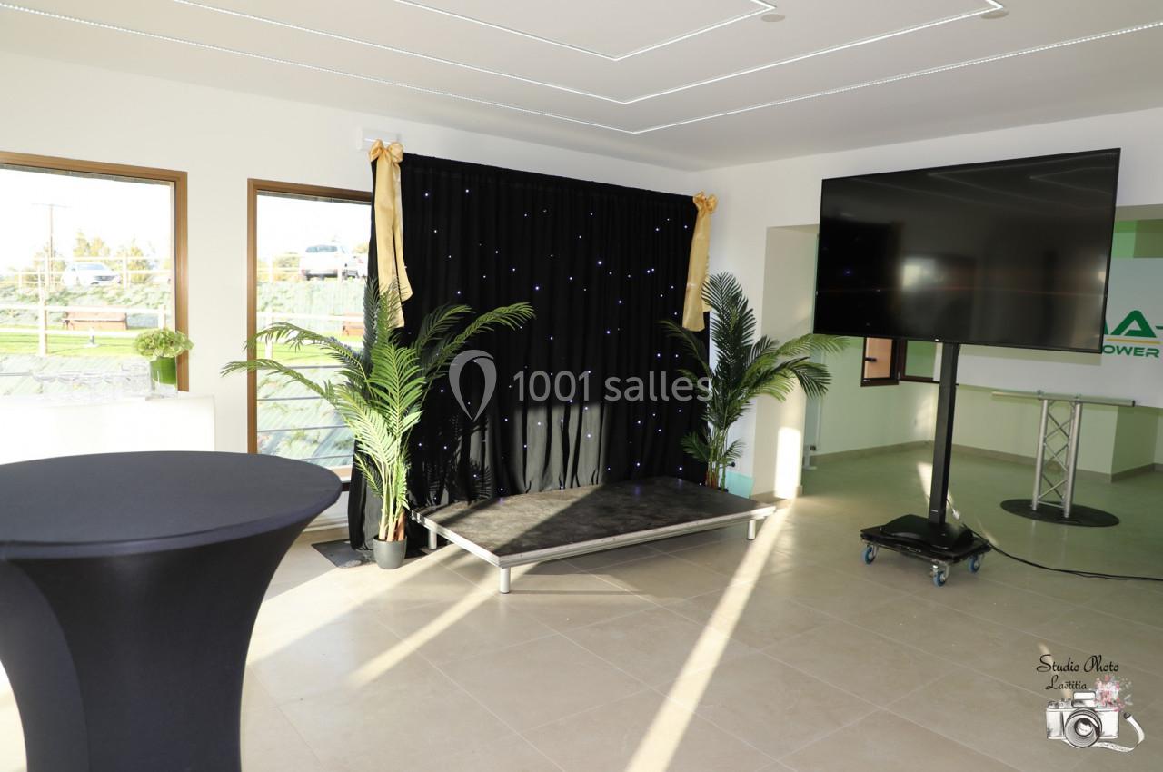 Location salle Saint-Samson-de-la-Roque (Eure) - Manoir Néo Normand #93 Espace intérieur lumineux avec une petite scène, rideau noir étoilé, écran sur pied et plantes décoratives.