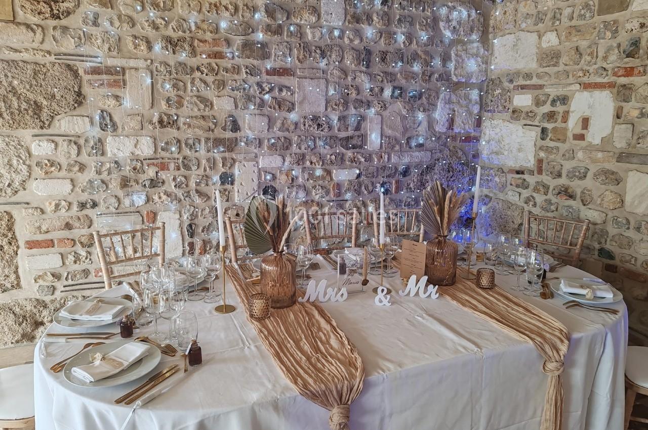 Location salle Saint-Samson-de-la-Roque (Eure) - Manoir Néo Normand #7 Table décorée pour un mariage avec nappes beige, vaisselle élégante, bougies et ornements devant un mur en pierre.