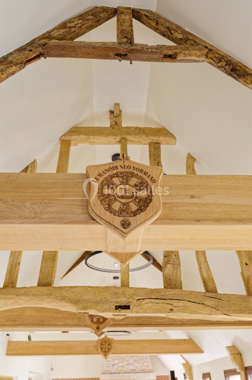 Charpente en bois apparente avec poutres anciennes et un blason gravé suspendu au centre.
