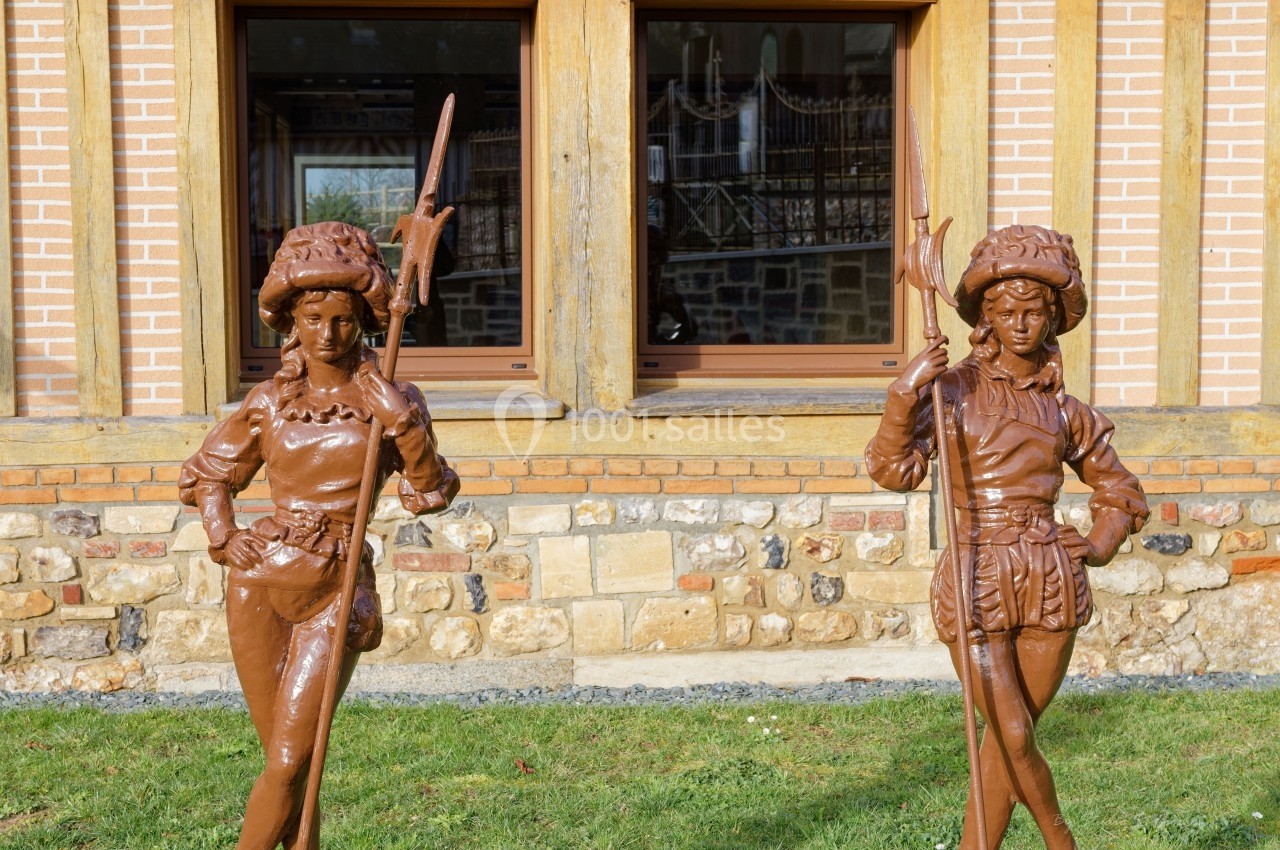 Deux statues en métal représentant des personnages médiévaux devant un bâtiment en briques et pierres.