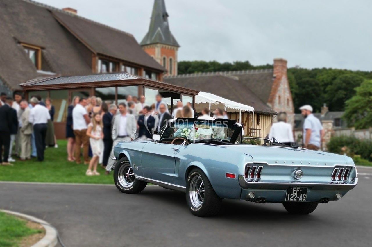 Voiture décapotable ancienne bleue garée devant un bâtiment en pierre, avec des invités rassemblés à l'arrière-plan.