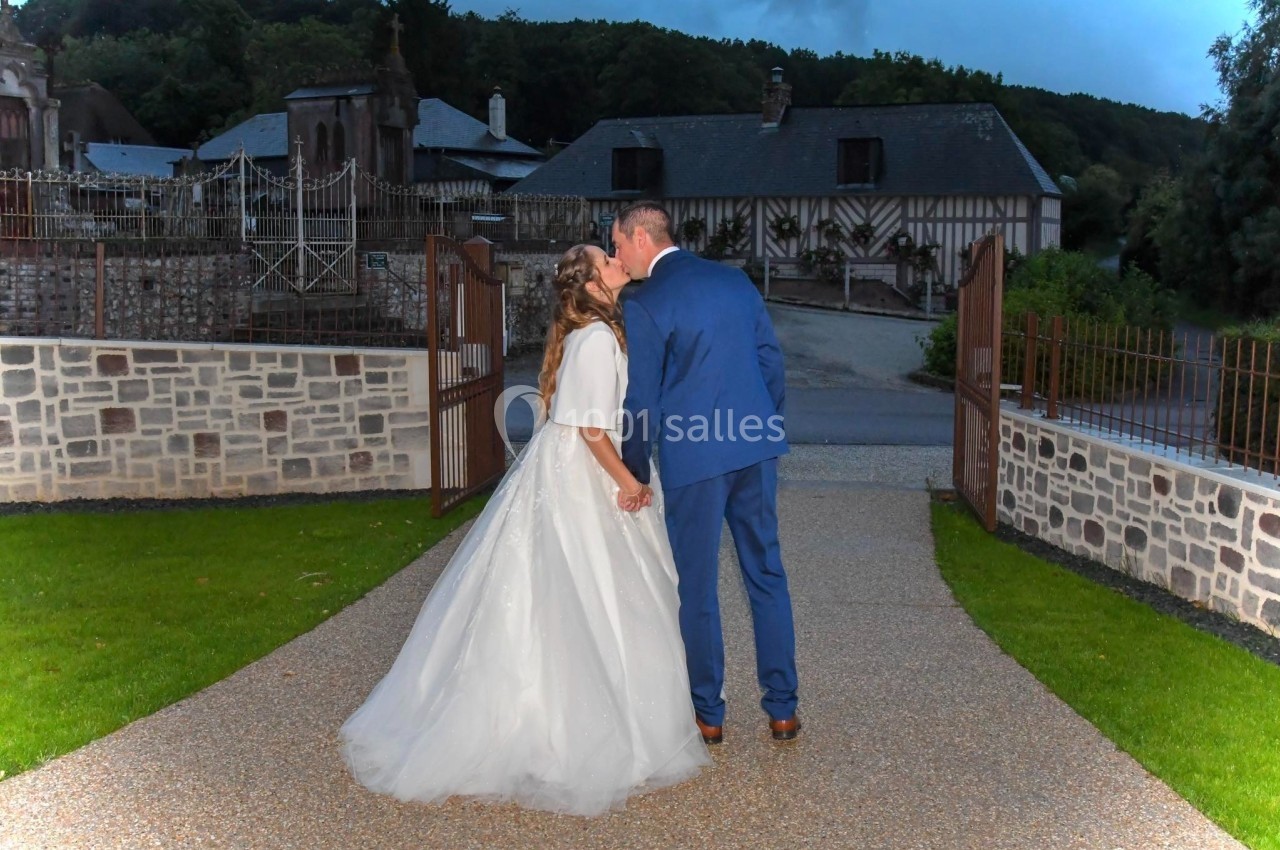 Un couple en tenue de mariage s'embrasse dans une allée pavée devant des bâtiments à colombages.
