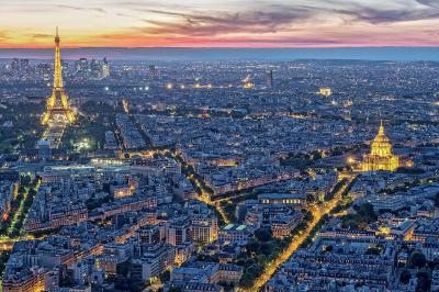 Vue aérienne de Paris au crépuscule, avec la tour Eiffel illuminée et les Invalides visibles au premier plan.