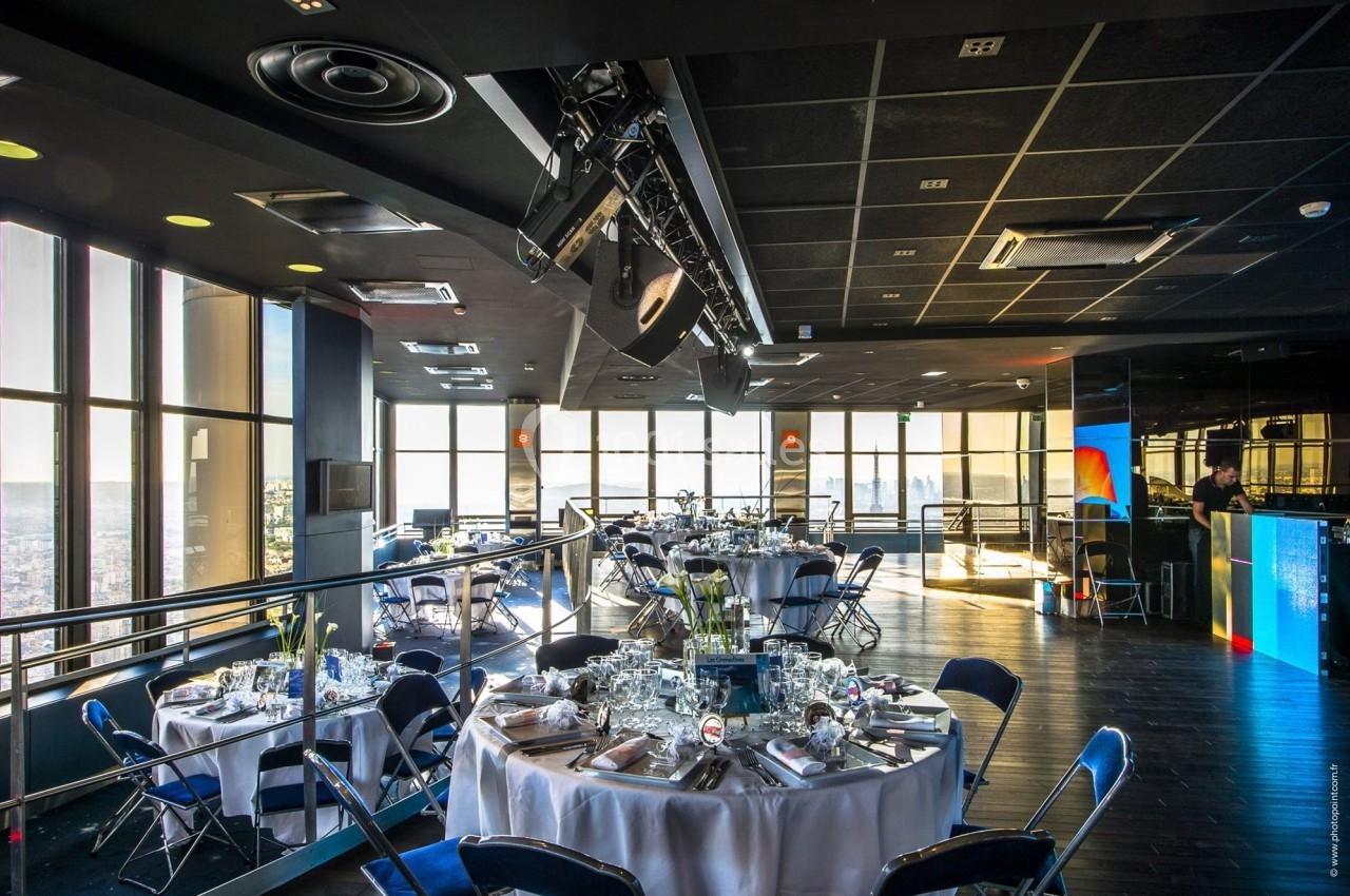 Salle de réception moderne avec tables dressées, grandes baies vitrées offrant une vue panoramique sur la ville.