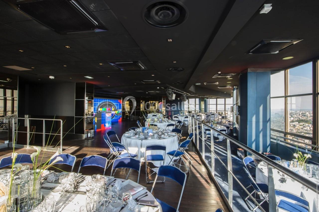 Salle de réception moderne avec tables rondes dressées, grandes baies vitrées et vue panoramique sur la ville.