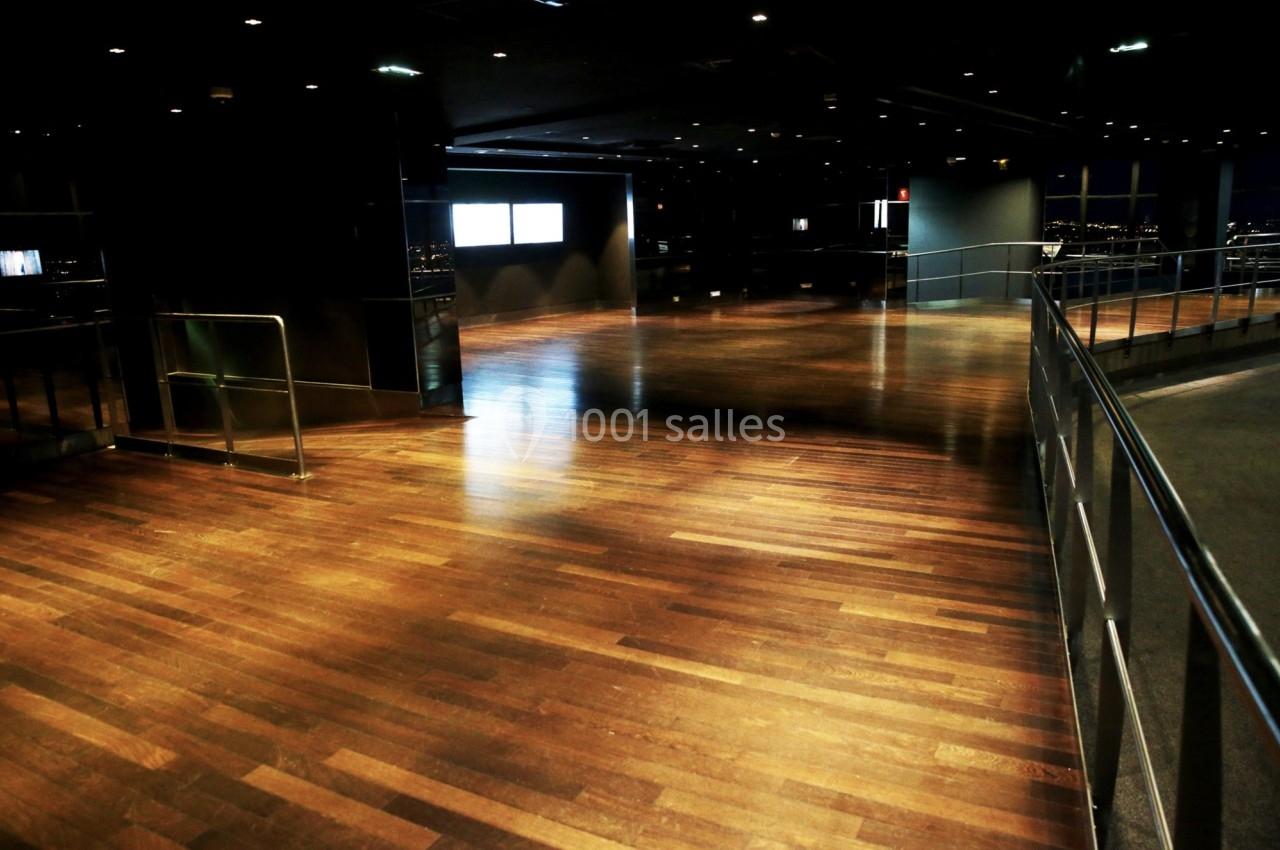 Salle vide avec un sol en parquet brillant, des rampes métalliques et des écrans lumineux en arrière-plan.