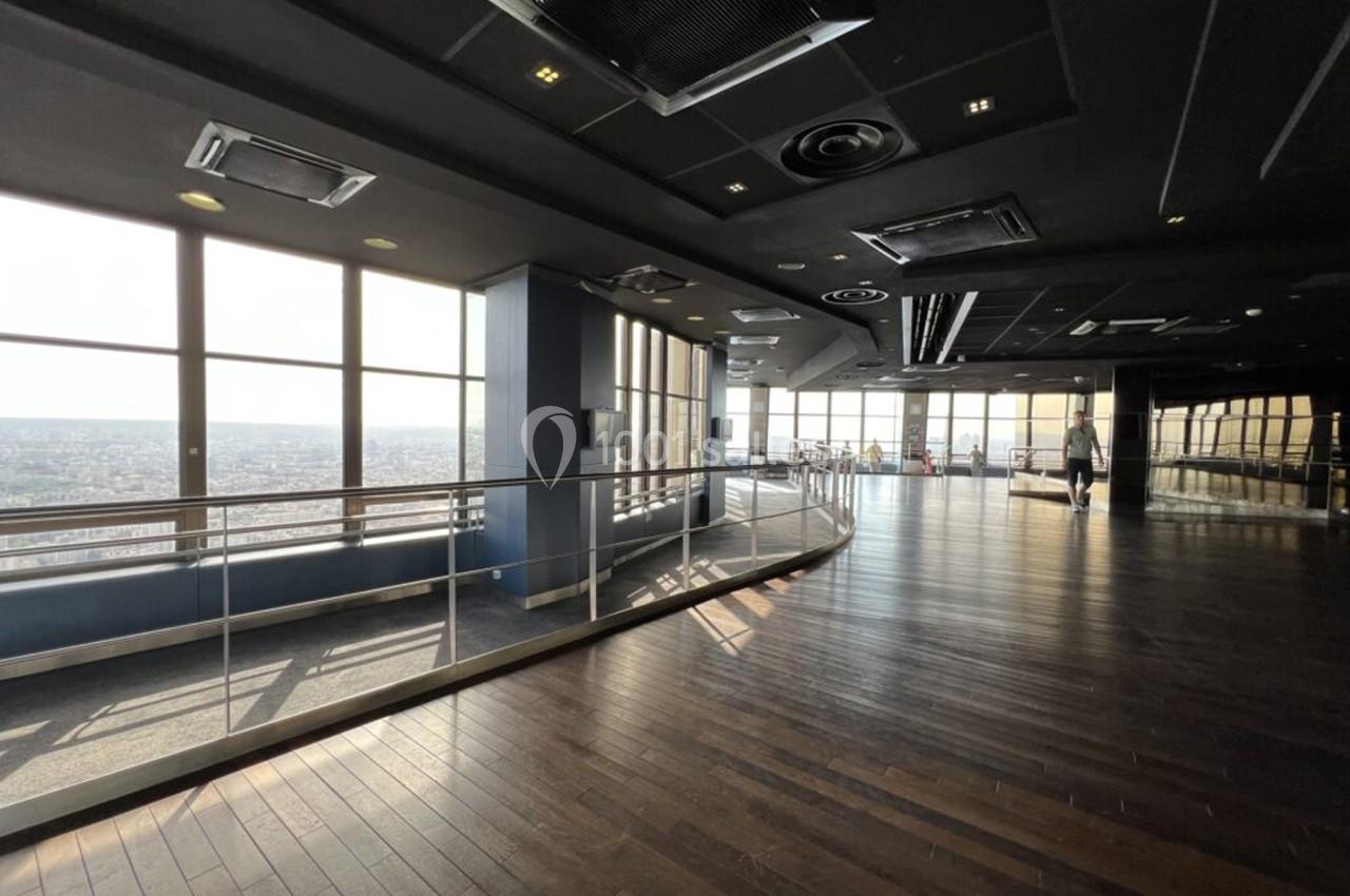 Intérieur d'un étage panoramique avec grandes baies vitrées, parquet en bois et garde-corps métallique.