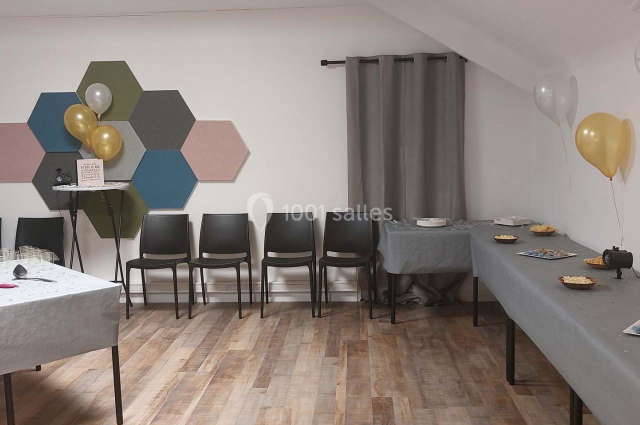 Salle décorée pour un événement avec ballons dorés, tables dressées avec des snacks et chaises alignées contre un mur.