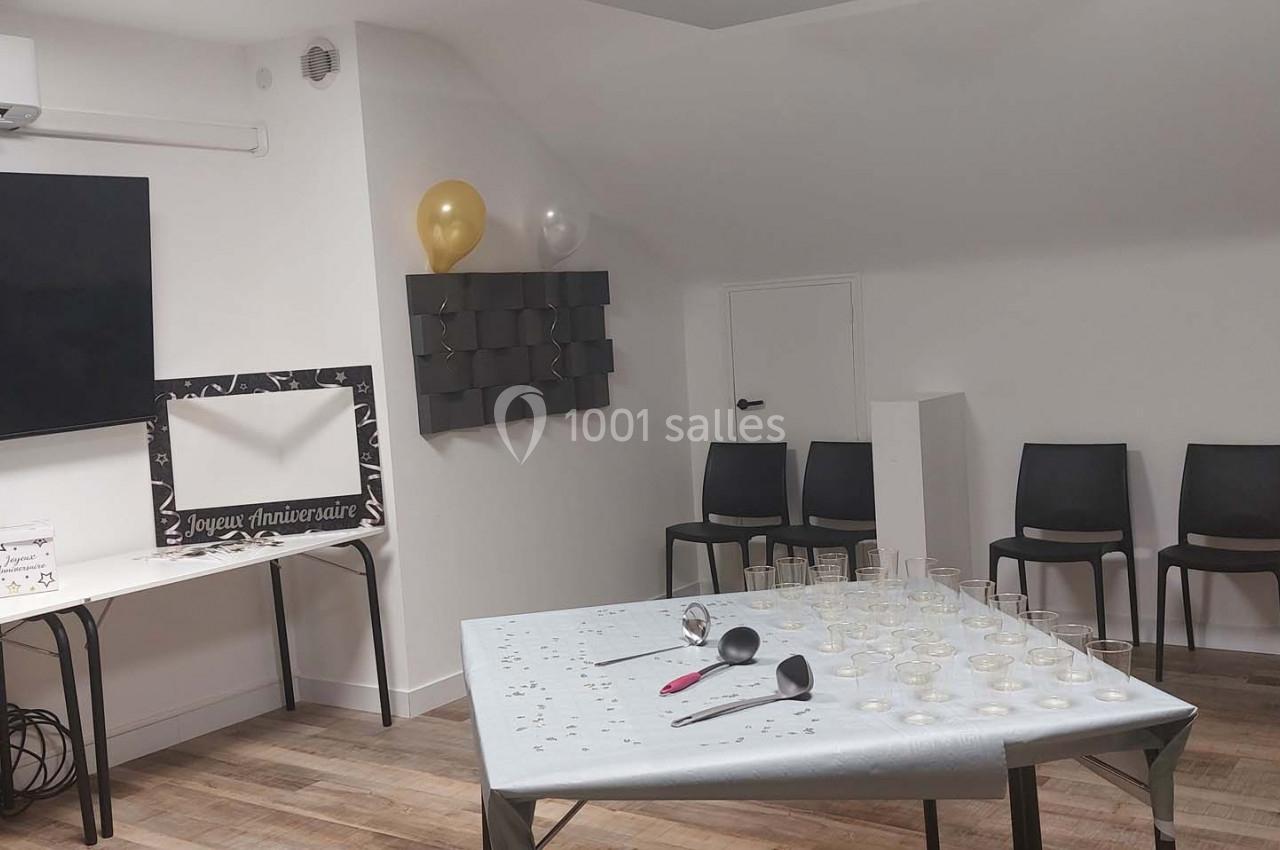 Salle aménagée avec des chaises, une table avec des verres et accessoires, un écran mural et des décorations discrètes.