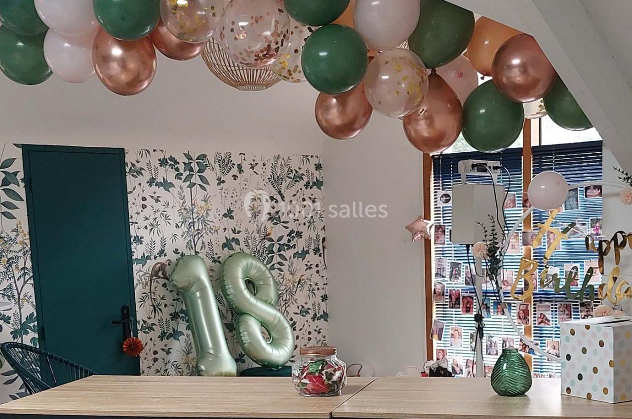 Décoration d'anniversaire avec ballons verts, blancs et dorés, chiffres ’18’ gonflés et guirlandes dans une pièce lumineuse.