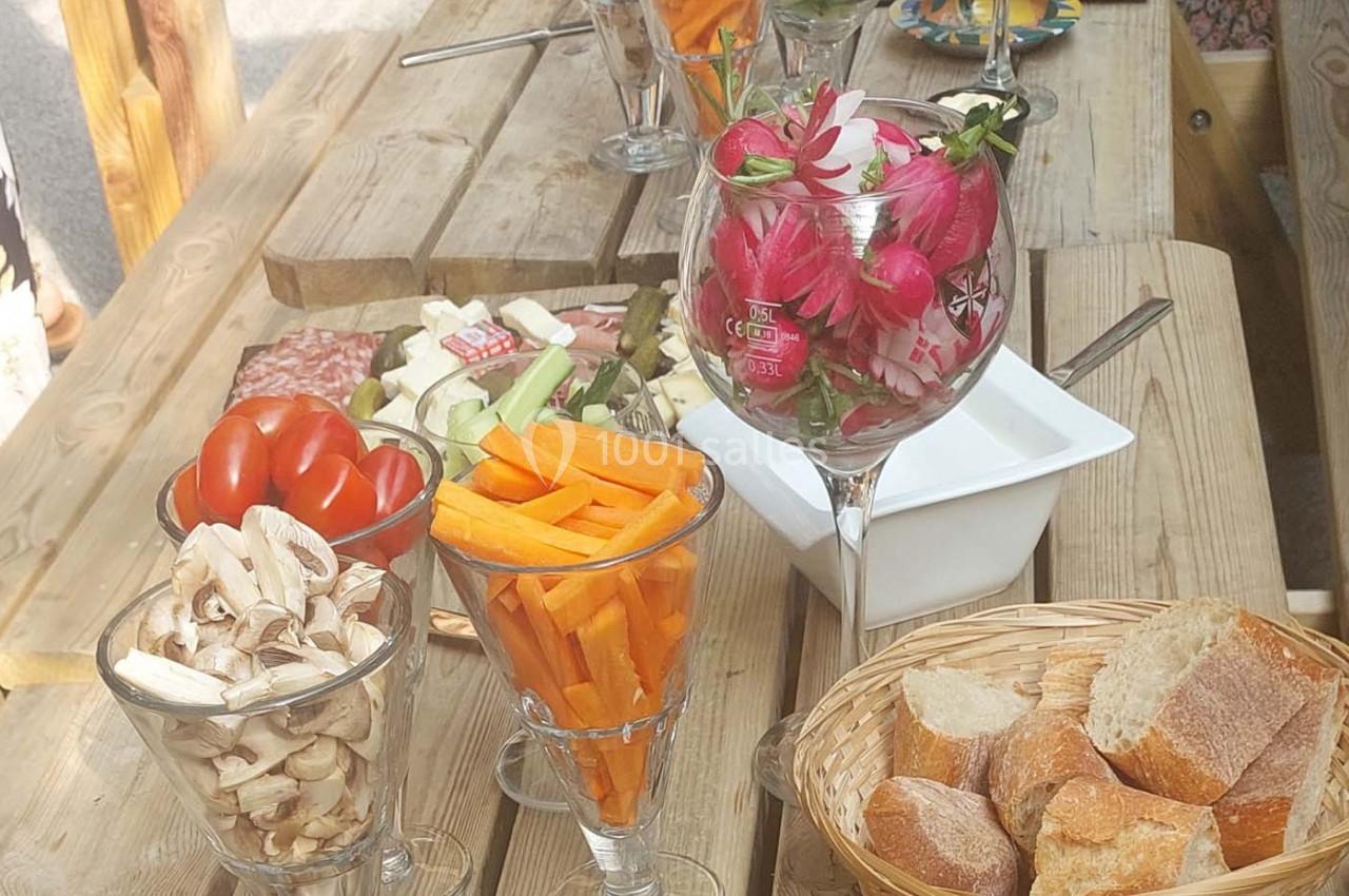 Assortiment de légumes frais, radis et pain disposés sur une table en bois pour un apéritif en plein air.
