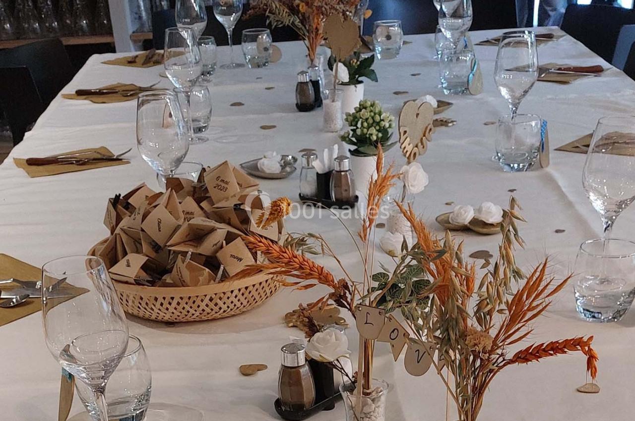 Table décorée pour un événement avec nappes blanches, verres, fleurs séchées et paniers contenant des petits sachets.