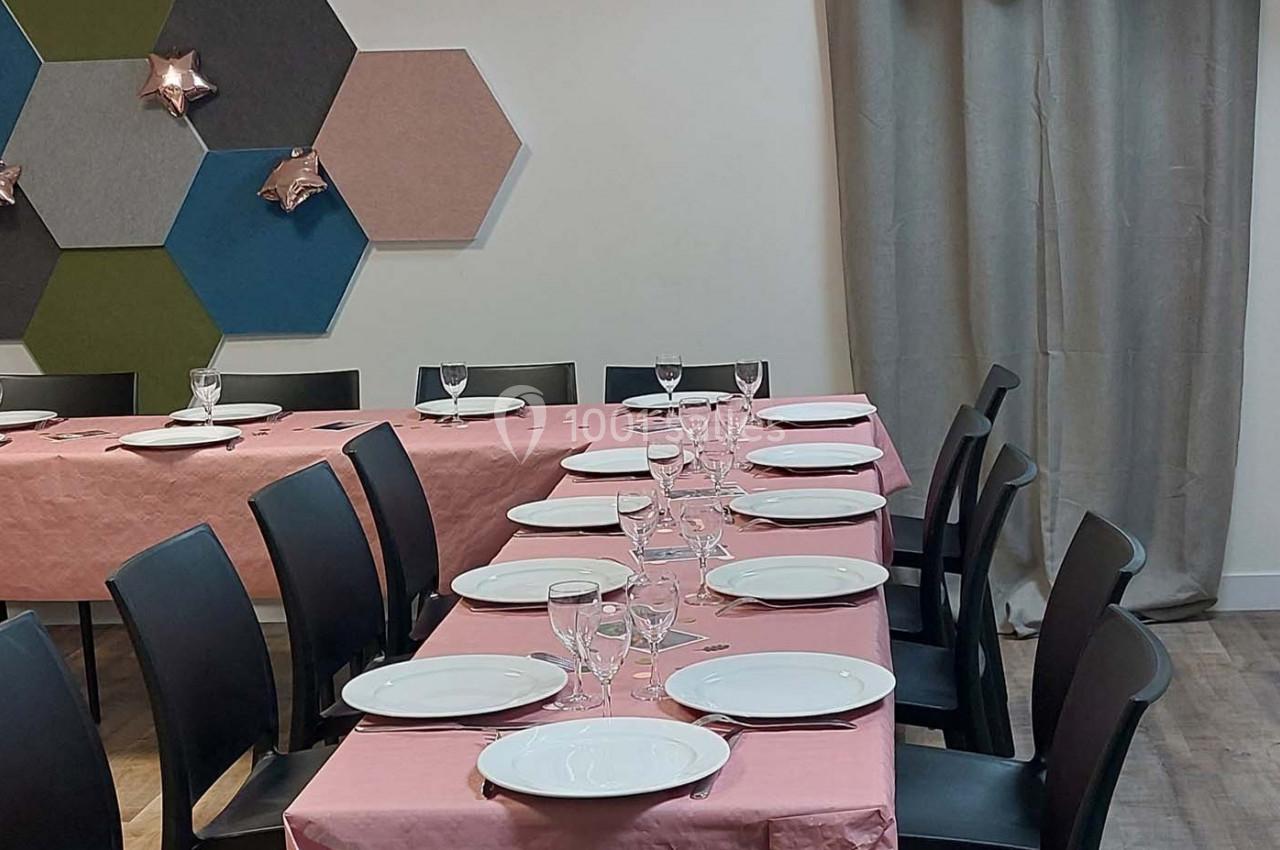 Tables dressées avec nappes roses, assiettes blanches et verres, dans une salle décorée de panneaux muraux colorés.