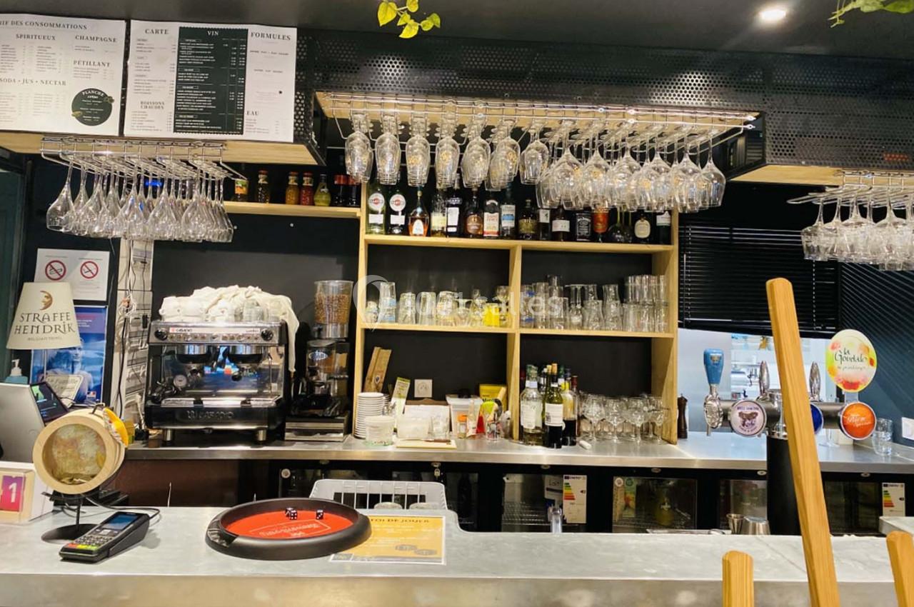 Comptoir de bar avec machine à café, verres suspendus, étagères de bouteilles et accessoires de service.