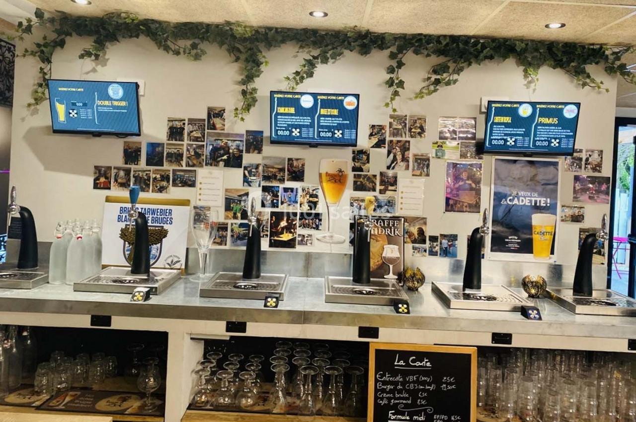 Comptoir de bar avec tireuses à bière, verres alignés, écrans d'affichage et décorations murales de photos.