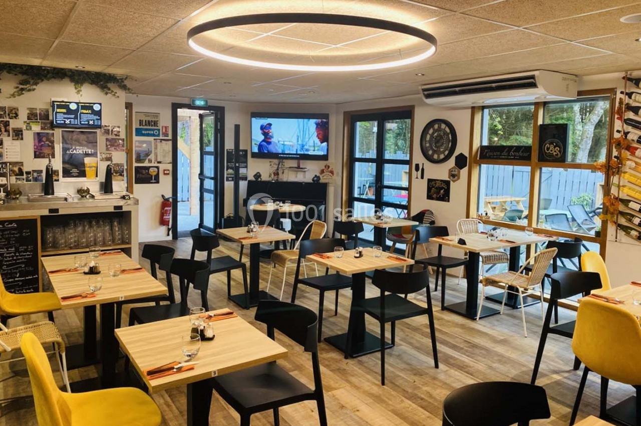Salle de restaurant moderne avec tables en bois, chaises colorées et grande baie vitrée laissant entrer la lumière naturelle.