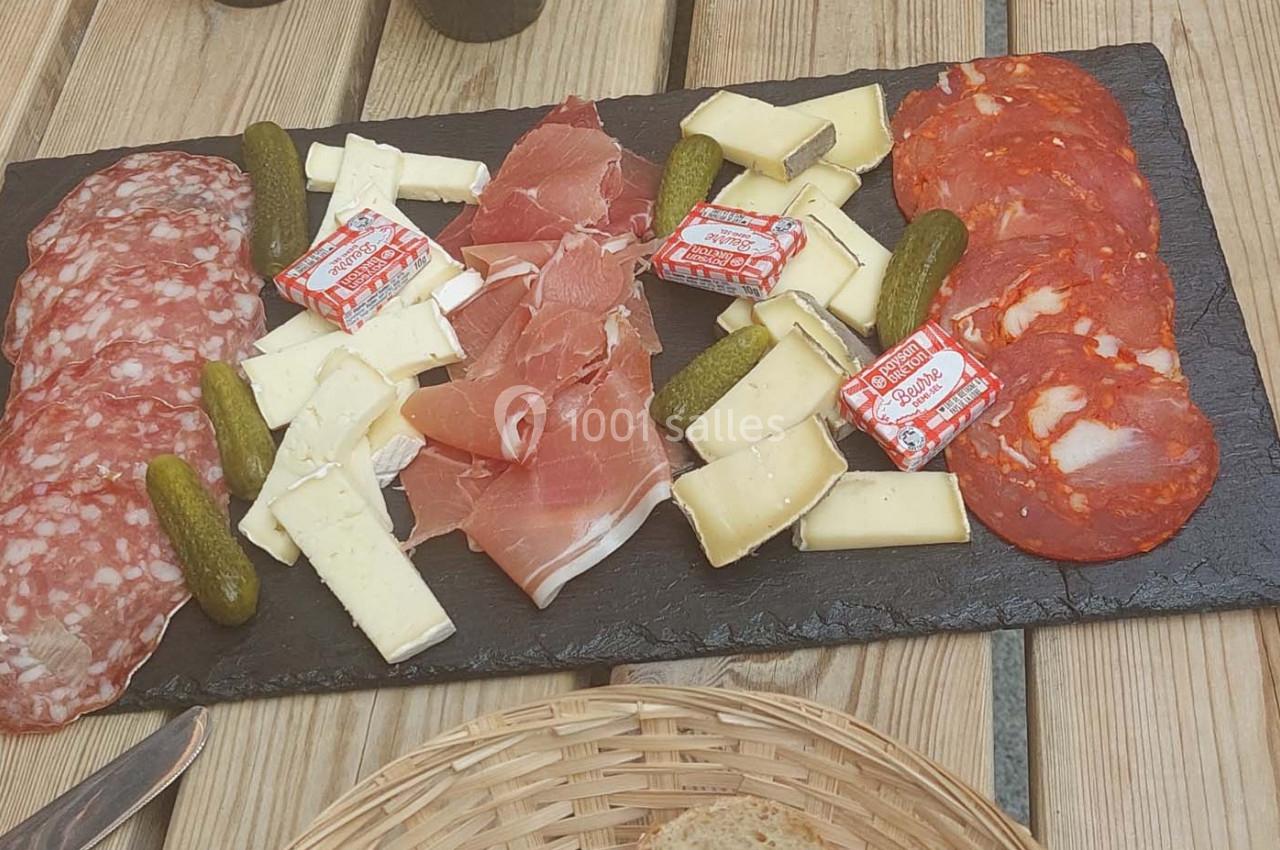 Plateau de charcuterie et fromages avec cornichons et portions de beurre, présenté sur une planche en ardoise.