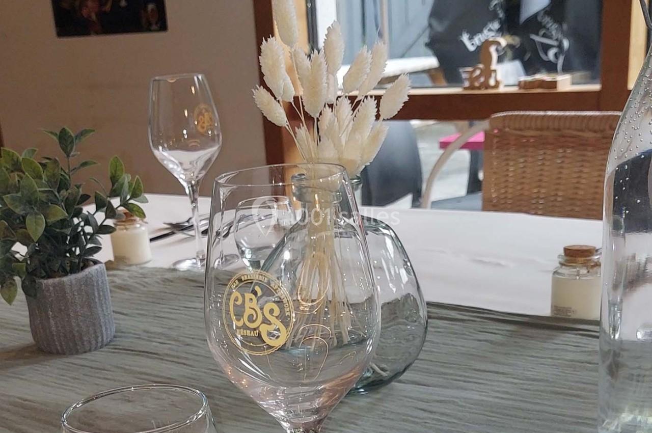 Table dressée avec des verres, une carafe, un bouquet de fleurs séchées et une petite plante en pot.