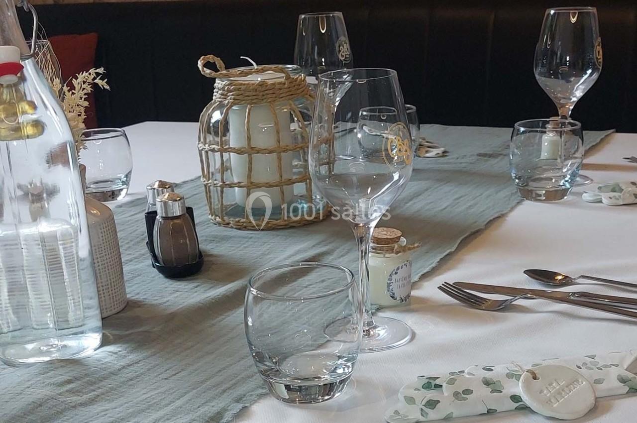Table dressée avec nappe blanche, chemin de table bleu, verres, couverts, bougies et bouteille d'eau.
