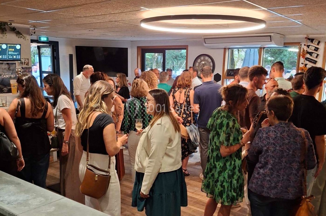 Groupe de personnes discutant dans une salle lumineuse avec des baies vitrées et un éclairage circulaire au plafond.