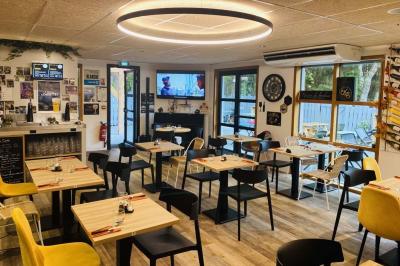 Salle lumineuse avec tables blanches, chaises noires, décoration murale hexagonale et coin détente avec fauteuil jaune.