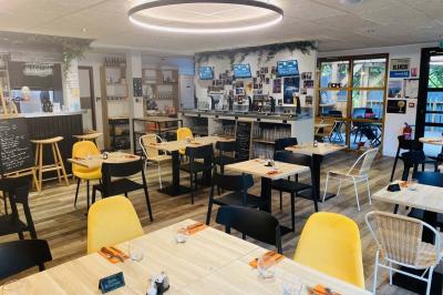 Salle lumineuse avec tables blanches, chaises noires, décoration murale hexagonale et coin détente avec fauteuil jaune.