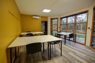 Salle lumineuse avec tables blanches, chaises noires, décoration murale hexagonale et coin détente avec fauteuil jaune.