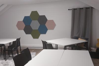 Salle lumineuse avec tables blanches, chaises noires, décoration murale hexagonale et coin détente avec fauteuil jaune.