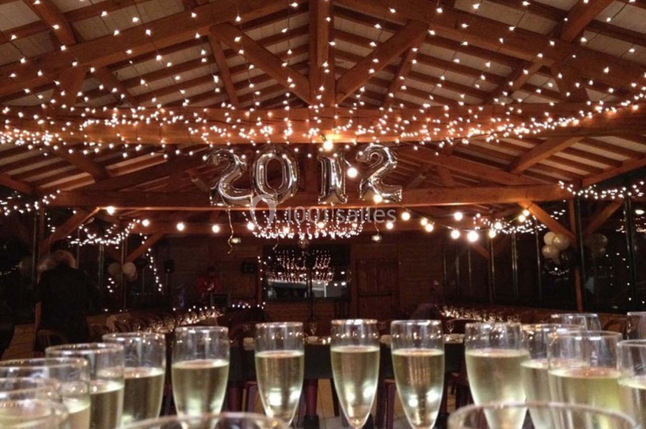 Salle décorée pour une fête avec guirlandes lumineuses, ballons ’2012’ et verres de champagne alignés au premier plan.