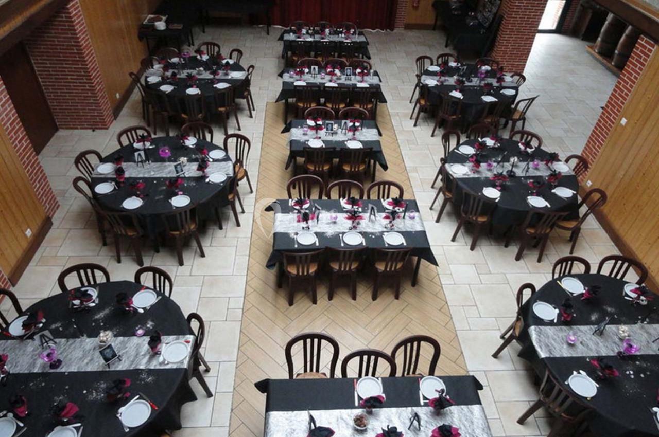 Salle de réception avec tables rondes dressées, nappes noires, chemins de table argentés et décorations florales.