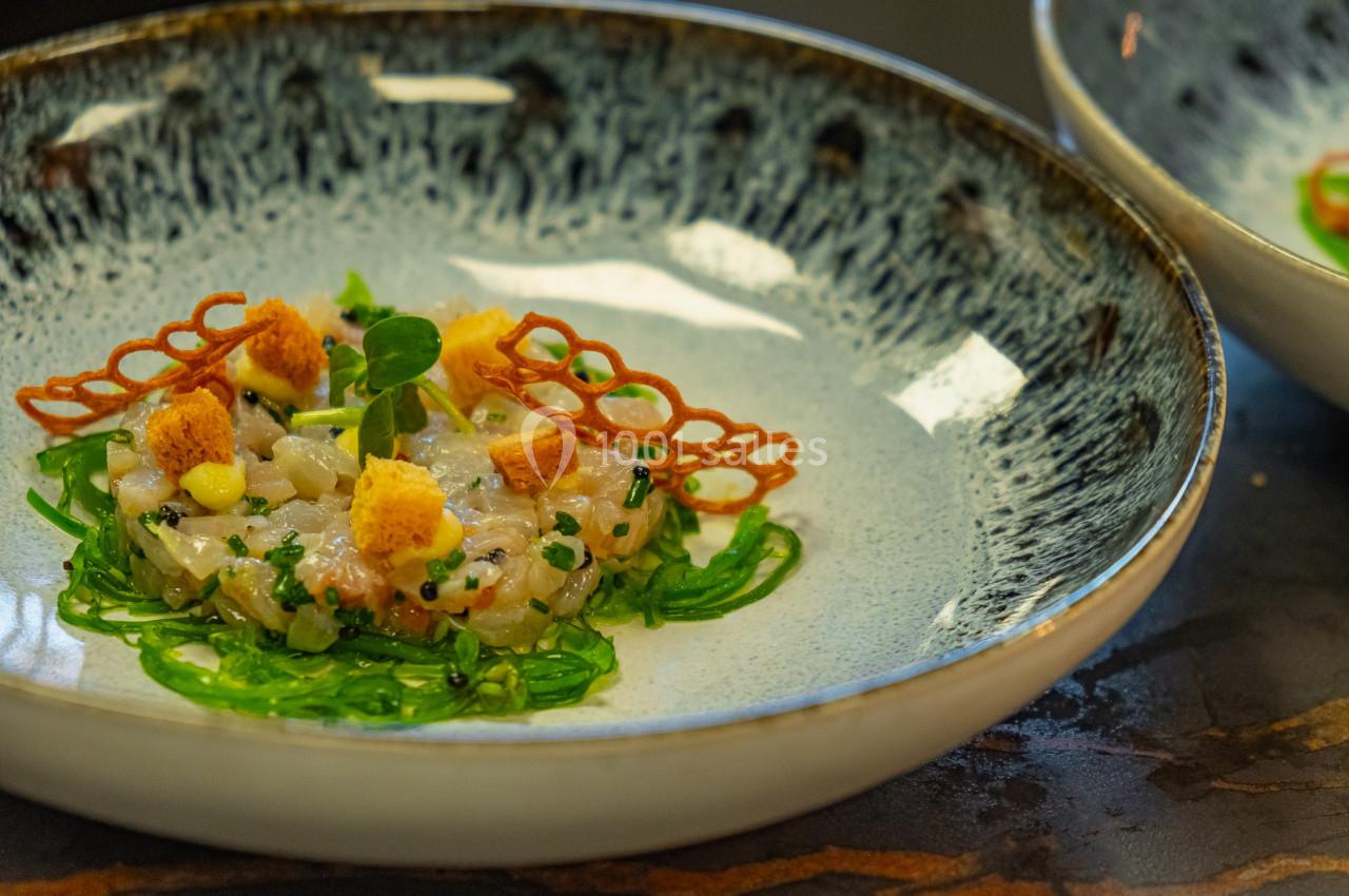 Tartare de poisson présenté avec algues, croûtons, décorations croustillantes et herbes fraîches dans une assiette.