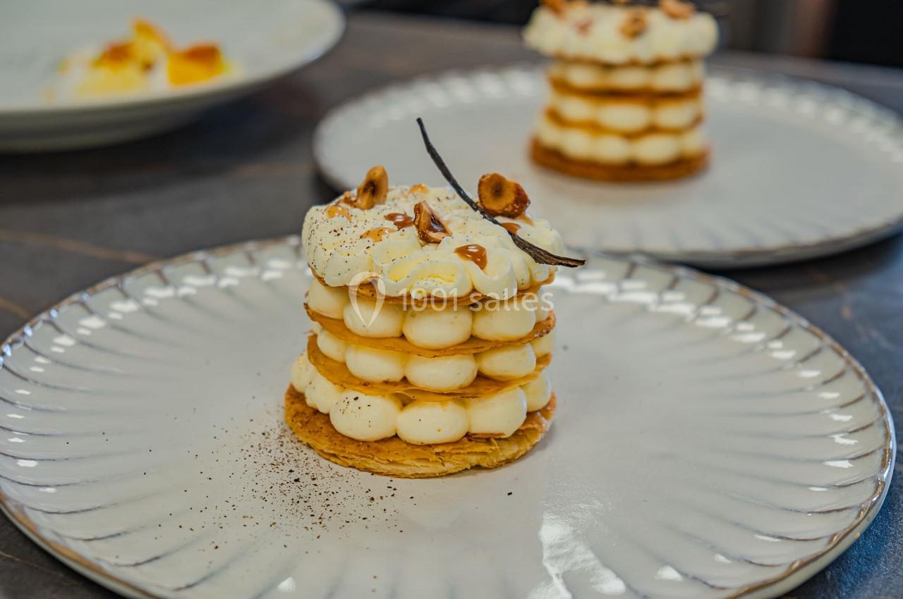 Dessert composé de couches de pâte feuilletée, crème vanillée, noisettes et gousse de vanille en décoration.