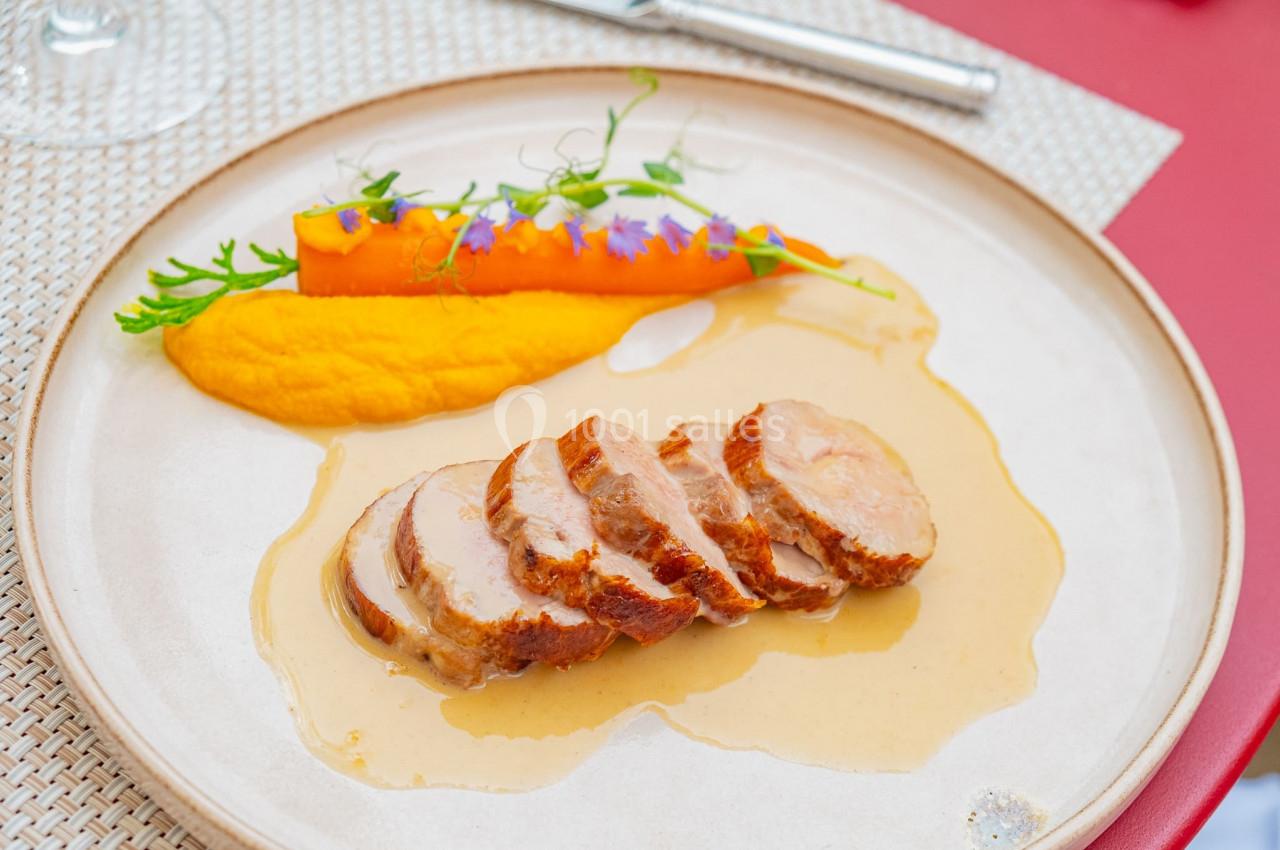 Assiette avec des tranches de viande nappées de sauce, purée de carotte et garniture de légumes et fleurs comestibles.