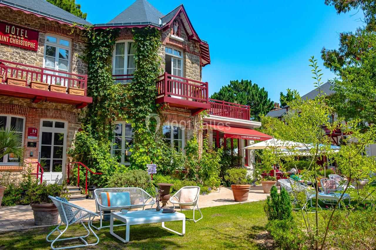 Façade d'un hôtel en briques avec balcons rouges, entouré de verdure et d'un jardin aménagé avec mobilier de jardin.