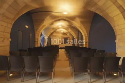 Salle voûtée avec murs en pierre, tables et chaises modernes, buffet en arrière-plan et éclairage chaleureux.
