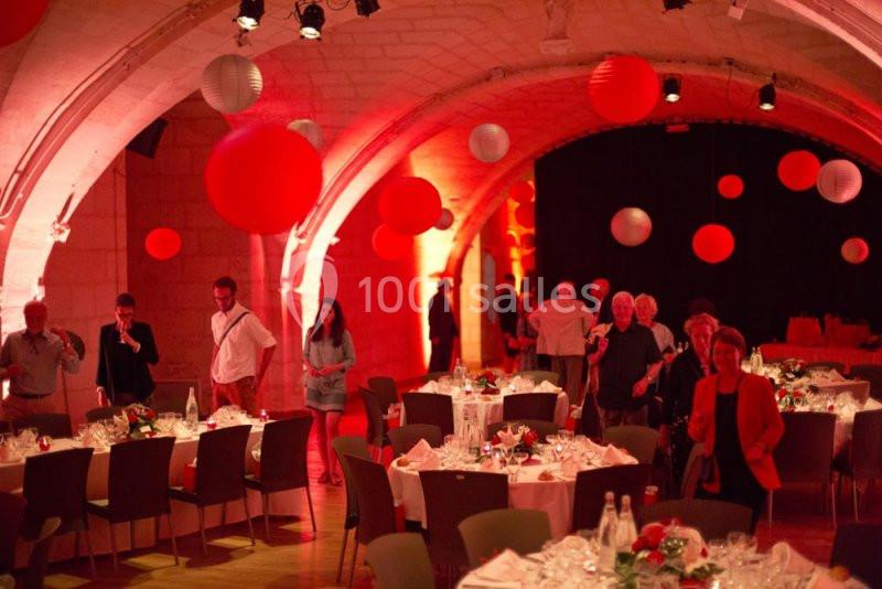 Salle voûtée décorée de lanternes rouges, avec des tables dressées et des invités en tenue de soirée.